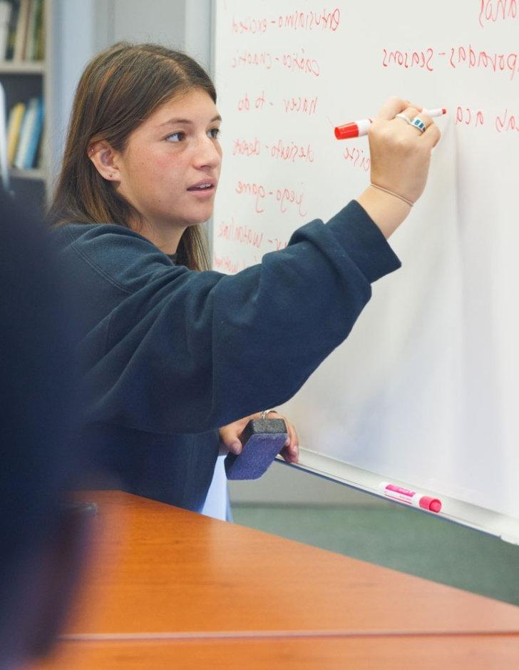 A student writes Spanish words on a whiteboard.